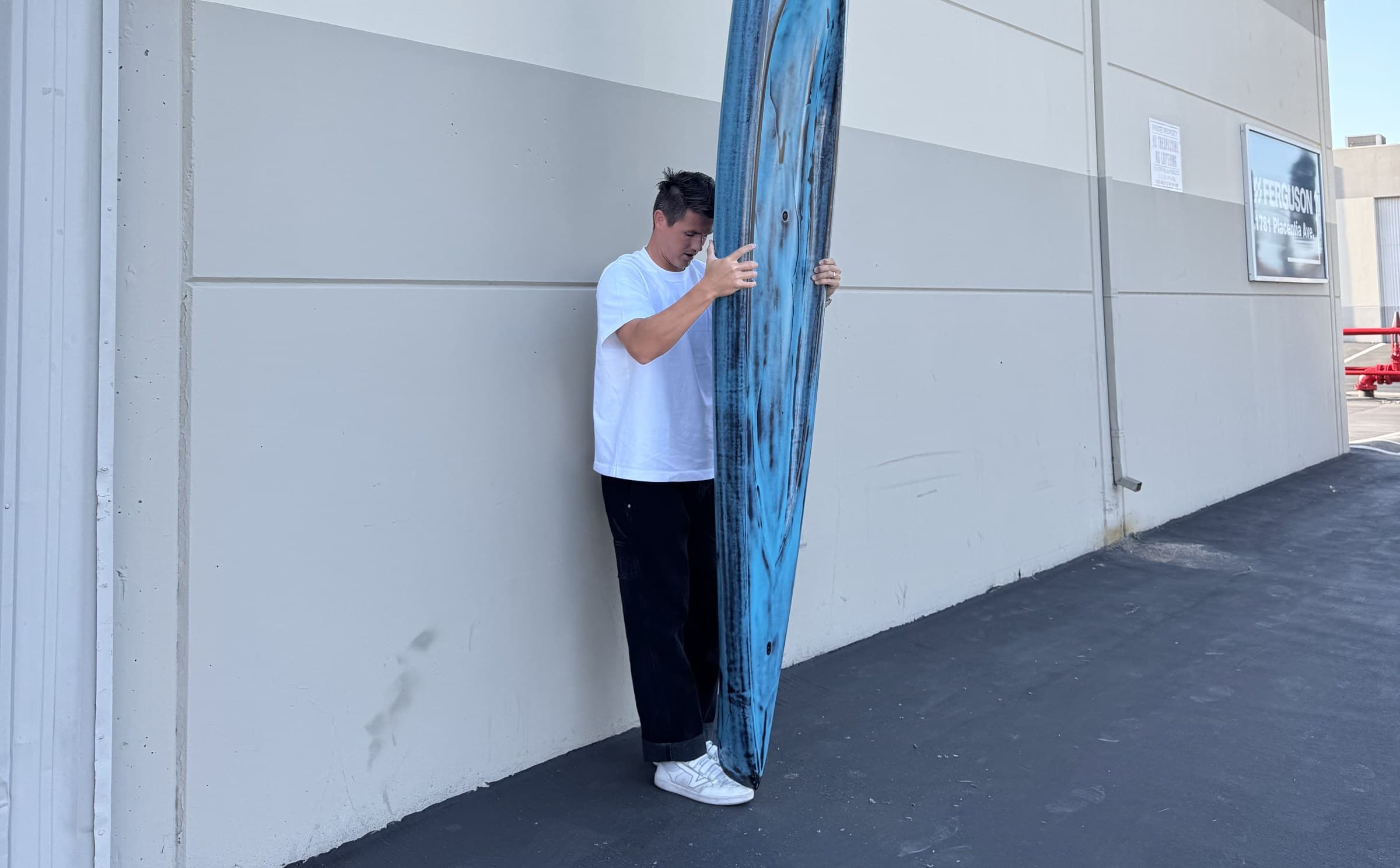 A custom Lundquist prone paddleboard standing against the shop wall, tail on the deck, nose overhead.